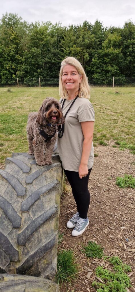 Michelle smiling standing beside her dog Charlie on a large tire outdoors.