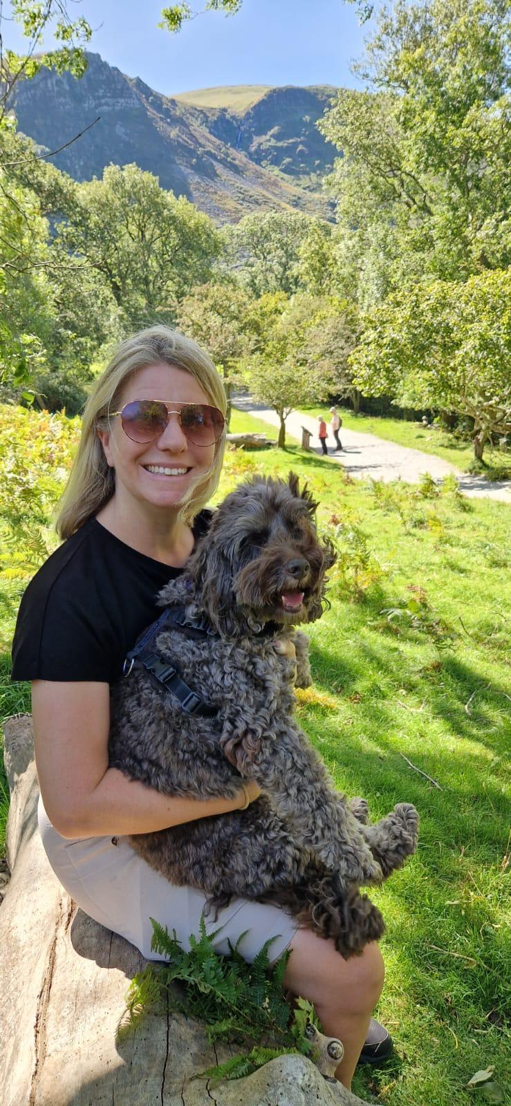 Michelle in sunglasses holding a happy dog in a sunny mountain park.